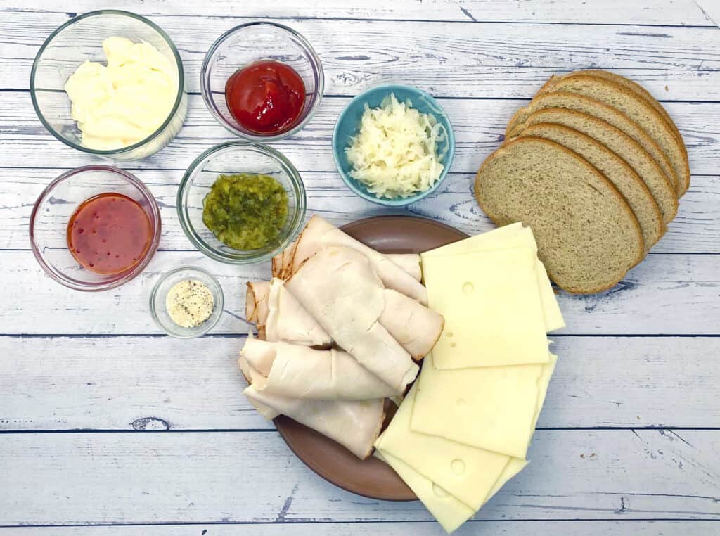 ingredients for turkey reuben sandwich - rye bread, deli turkey, swiss cheese, sauerkraut and thousand island dressing