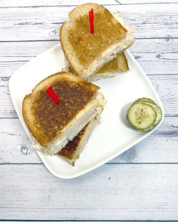 grilled turkey reuben sandwich on white plate with white wood background
