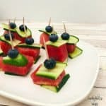 watermelon squares layered between slices of cucumber with a blueberry on top