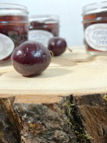 mason jars of cherries soaked in bourbon on a tree stump