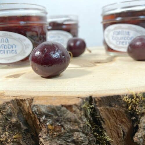 mason jars of cherries soaked in bourbon on a tree stump