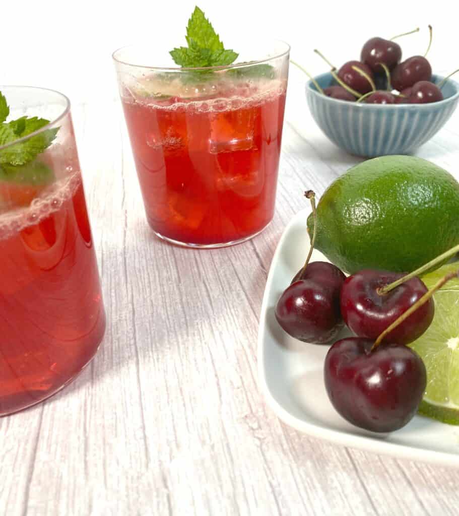 cherry bourbon lime cocktail in glasses with extra cherries and limes