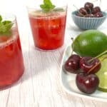 cocktail glasses filled with cherry juice, lime juice, bourbon and soda on a white wood background