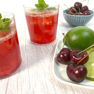 cocktail glasses filled with cherry juice, lime juice, bourbon and soda on a white wood background