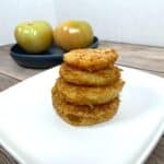 crispy, golden fried green tomatoes stacked four high on a white plate.