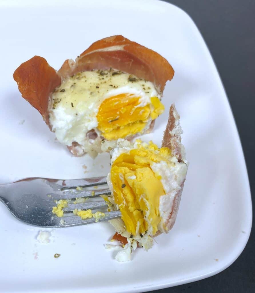 White plate - prosciutto egg cup is cut in half, showing the soft boiled yolk inside. 