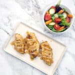 baked chicken breasts covered with spicy bbq drizzle next to a garden salad on a marble background