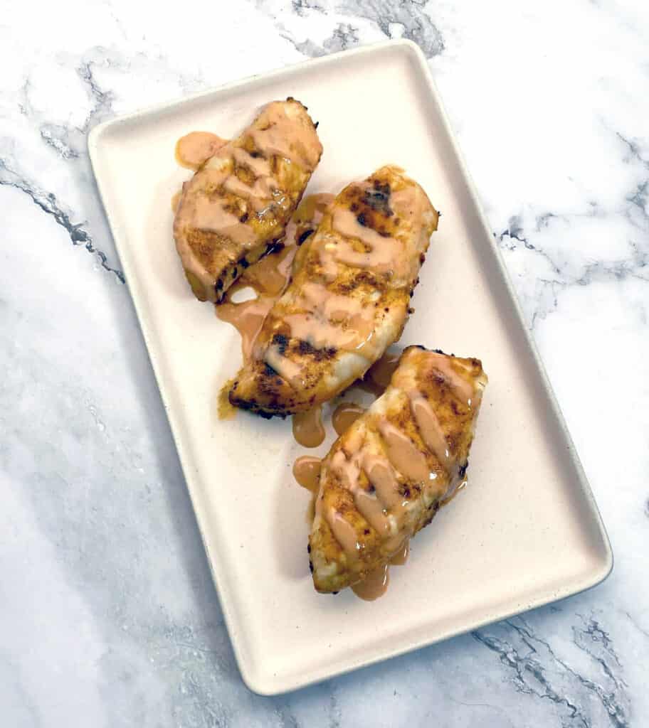 baked chicken breast drizzled with spicy bbq sauce, sitting on a rectangle platter with a marble background