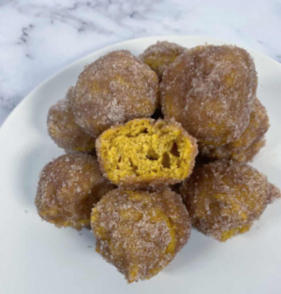 baked pumpkin donut holes stacked up with a bite missing from one