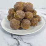 baked pumpkin donut bites covered in cinnamon sugar on white plate, marble background