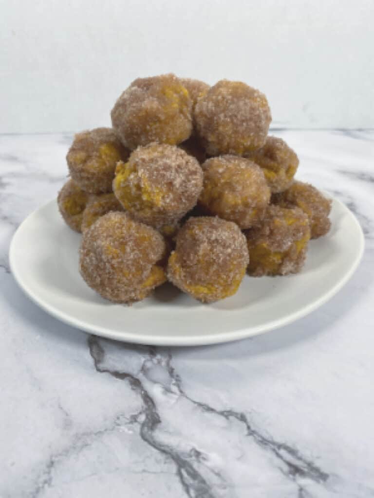 baked pumpkin donut bites covered in cinnamon sugar on white plate, marble background