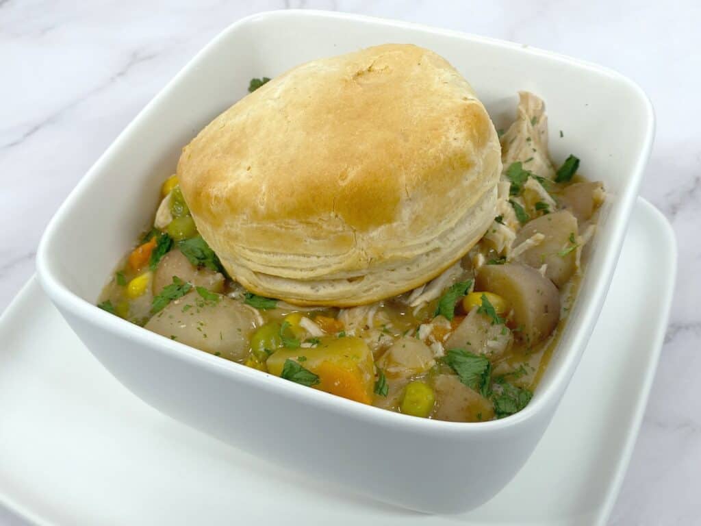 creamy chicken pot pie in a white, square bowl with a browned biscuit on top