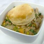 creamy chicken pot pie in a white, square bowl with a browned biscuit on top