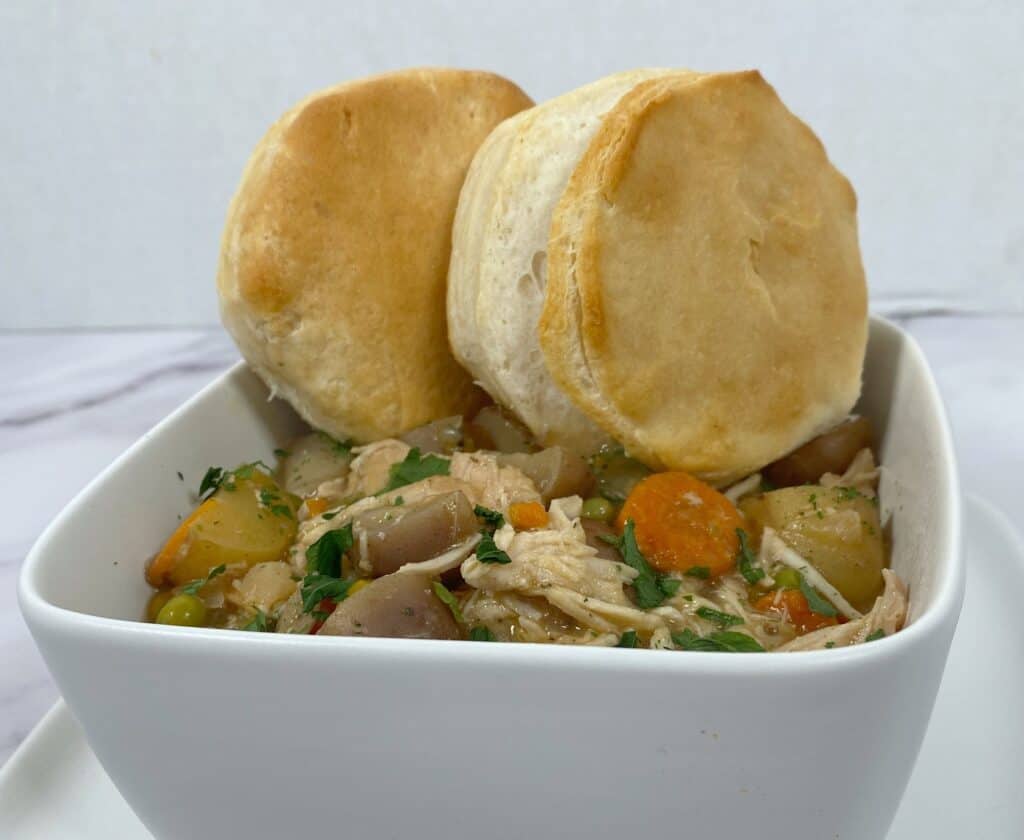 creamy chicken pot pie in a white, square bowl with a browned biscuit on top