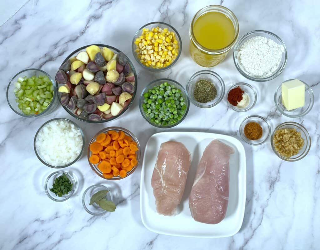 ingredients for chicken pot pie, including chicken breasts, carrots, potatoes, celery, peas, carrots and seasonings