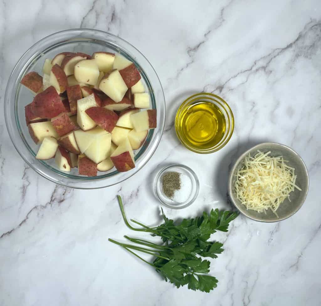 ingredients for parmesan parsley roasted potatoes - baby potatoes, olive oil, parmesan cheese, parsley, salt and pepper; on a marble background