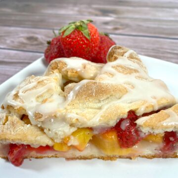 peaches and strawberries nestled in braided dough with a white glaze on top