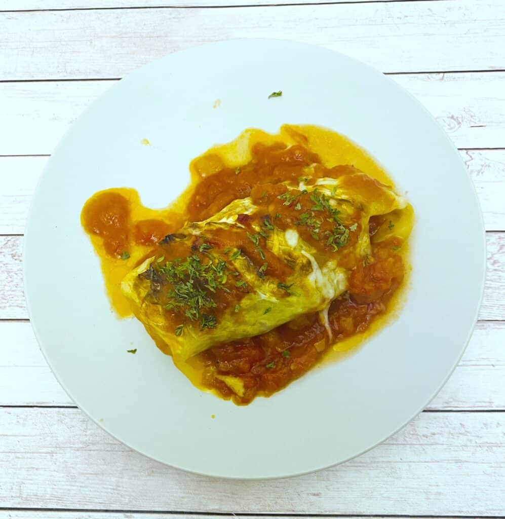 stuffed cabbage roll on top of tomato sauce on white plate 