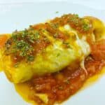 stuffed cabbage roll on white plate, tomato sauce underneath, sprinkling of parsley on top