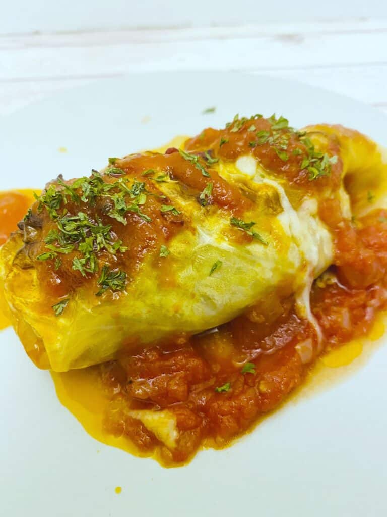stuffed cabbage roll on white plate, tomato sauce underneath, sprinkling of parsley on top