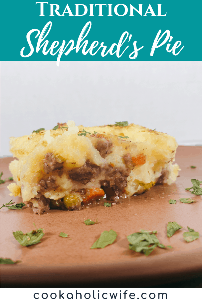 Slice of shepherd’s pie on a copper colored plate. Cheesy mashed potatoes are layered on top of a meat and veggie filling. The plate is garnished with parsley. 