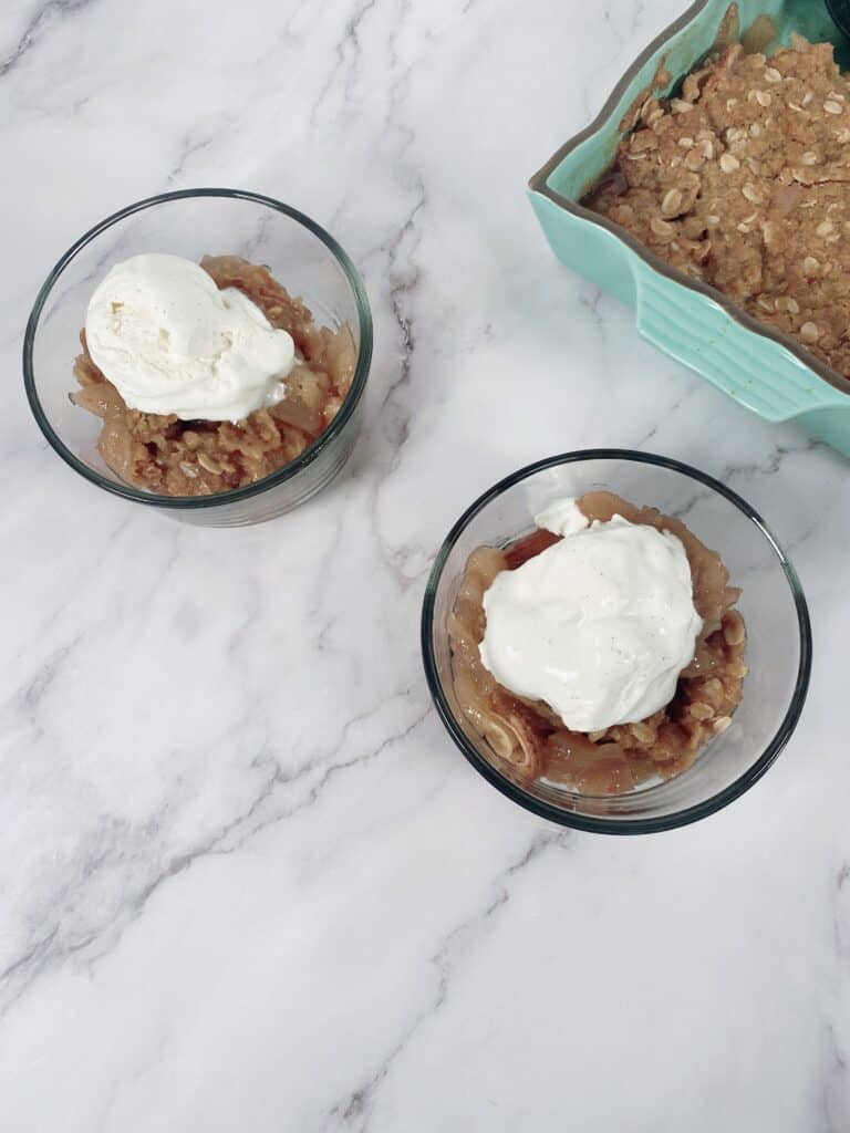 old fashioned apple crisp in glass bowl with scoop of vanilla ice cream on top