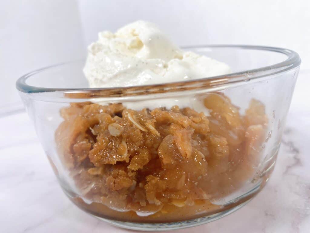 old fashioned apple crisp in a glass bowl with a scoop of vanilla ice cream on top