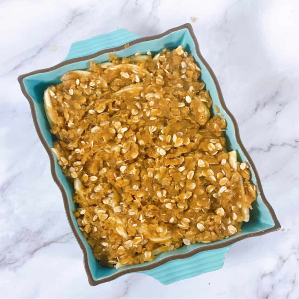 old fashioned apple crisp in a teal baking dish on a marble background