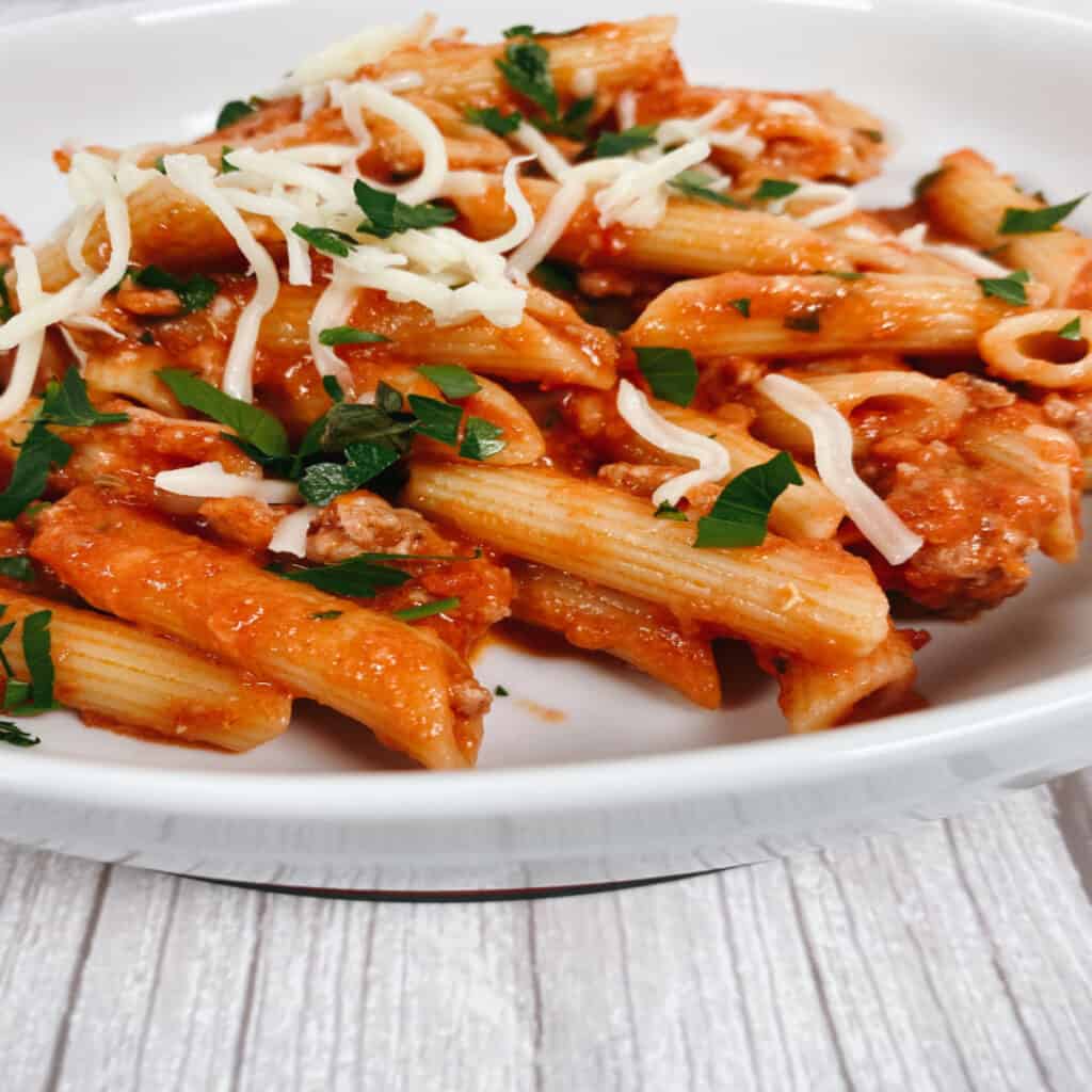 Bowl of penne with vodka sauce, topped with fresh parsley and cheese