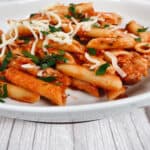 Bowl of penne with vodka sauce, topped with fresh parsley and cheese