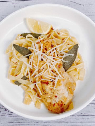 chicken cutlet on a bed of fettuccine pasta with fried sage leaves and a squeeze of lemon