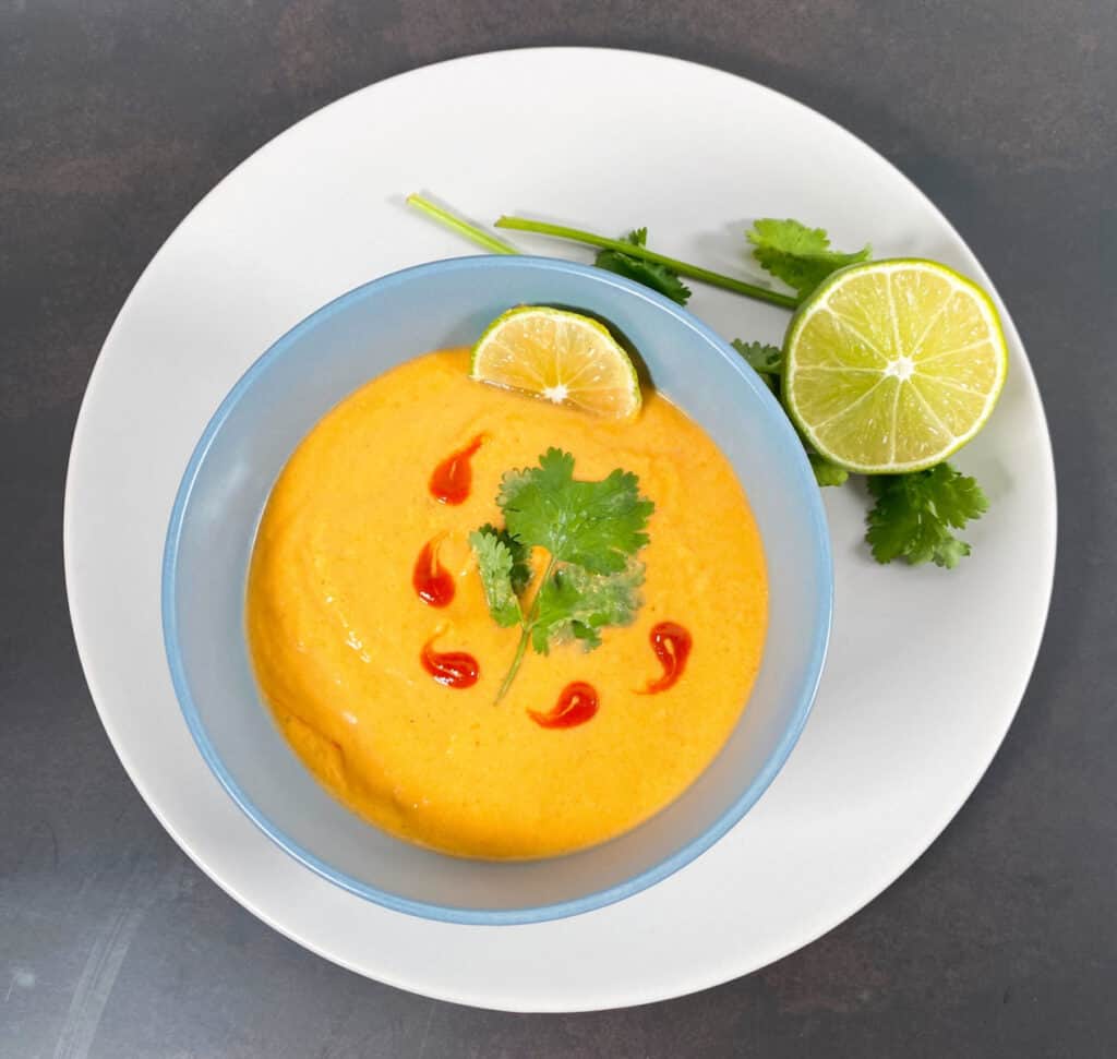 thai acorn squash soup pureed in bowl, garnished with cilantro leaves and sriracha