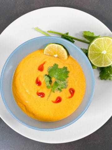 thai acorn squash soup pureed in bowl, garnished with cilantro leaves and sriracha