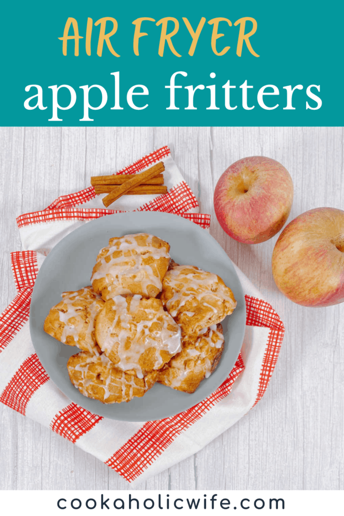 Air fryer apple fritters sit on a blue plate with a red and white checkered napkin. Apples and cinnamon sticks surround them. 