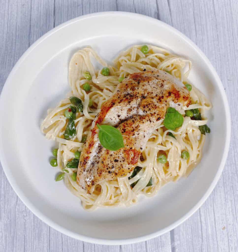 pan seared chicken sits on top a bed of pasta in a basil cream sauce