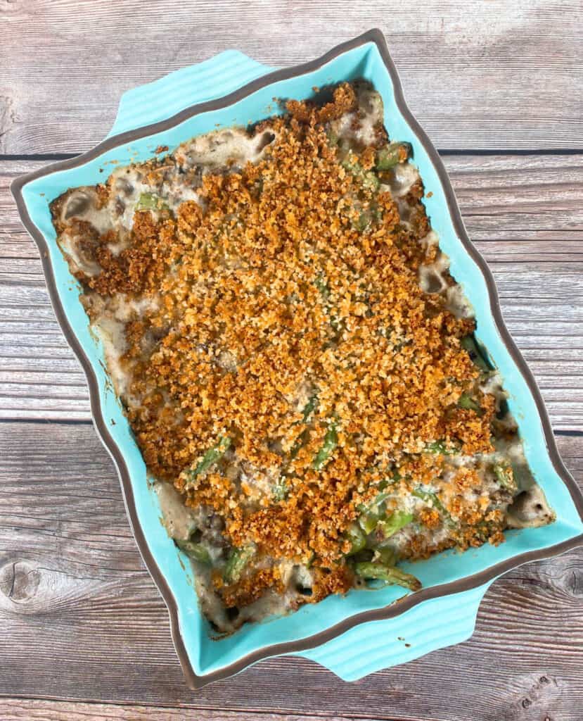 green bean casserole with a cheesy bread crumb topping in a teal casserole dish