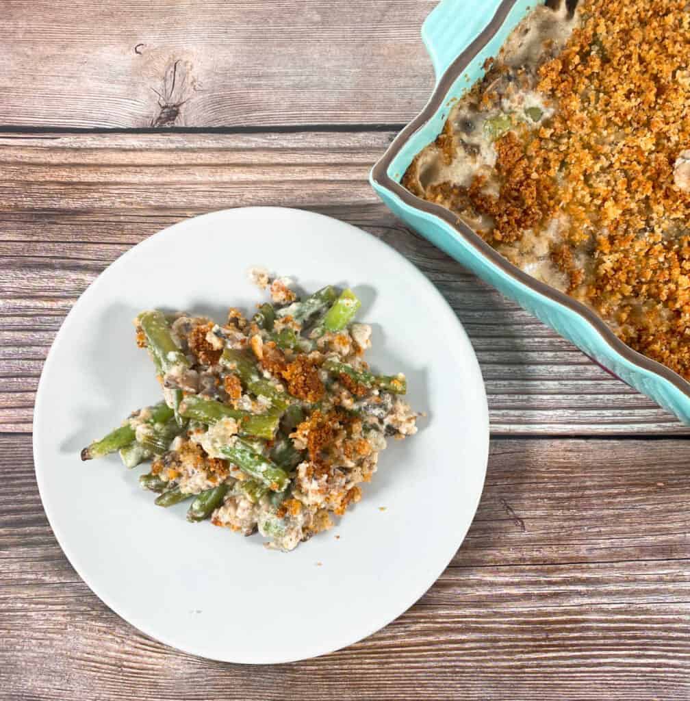 one serving lighter green bean casserole on a white plate with the teal casserole dish behind it