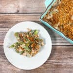 one serving lighter green bean casserole on a white plate with the teal casserole dish behind it