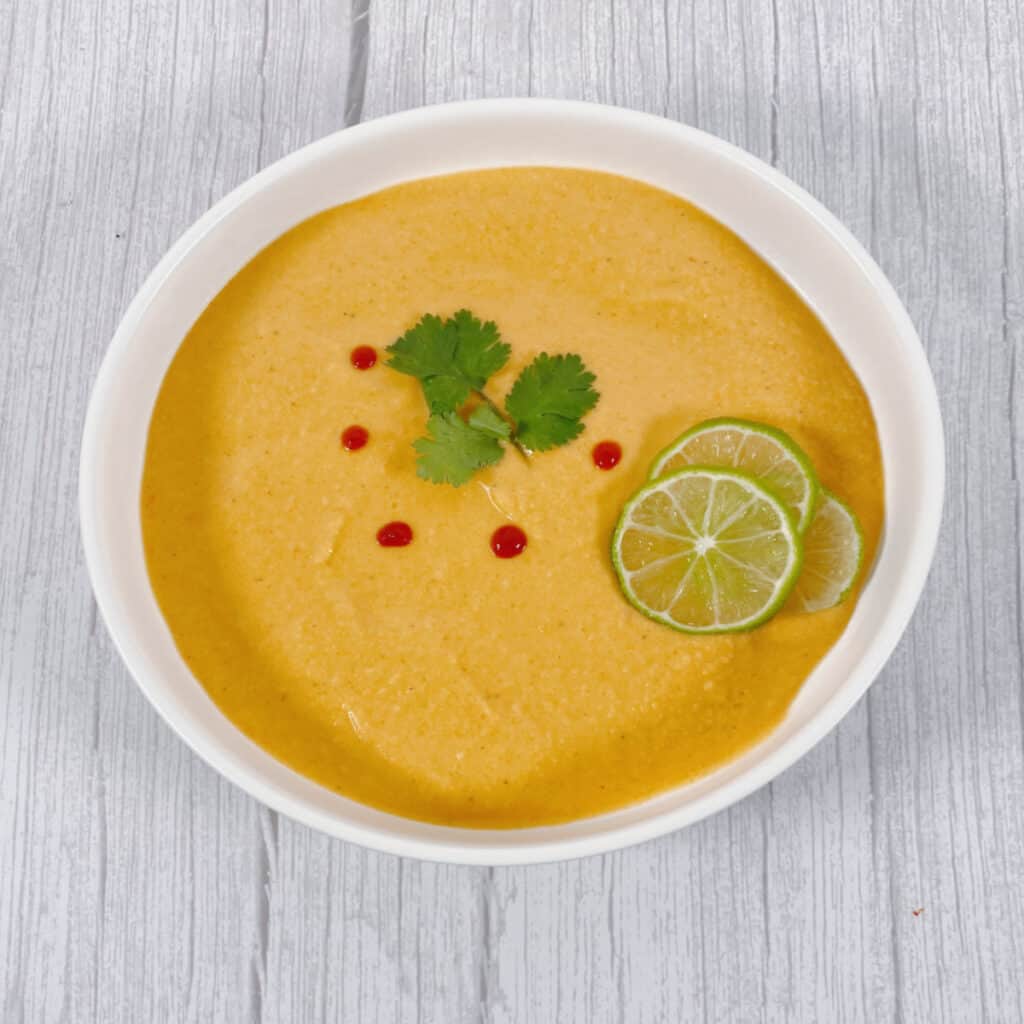 thai acorn squash soup pureed in bowl, garnished with cilantro leaves and sriracha