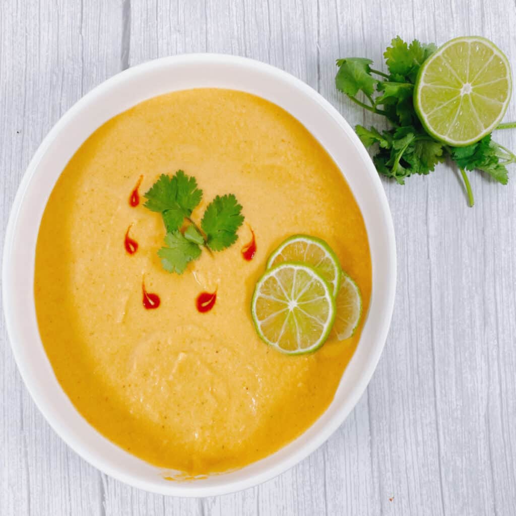 thai acorn squash soup pureed in bowl, garnished with cilantro leaves and sriracha