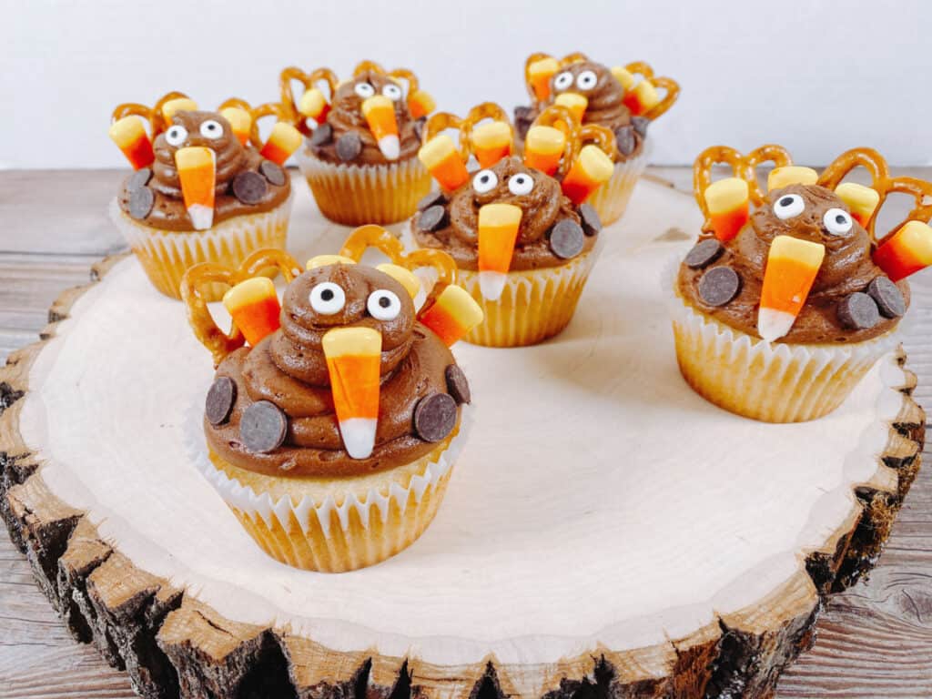 cupcakes are made into adorable thanksgiving turkeys by using pretzels, candy corn, chocolate chips and candy eyes