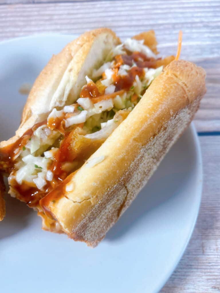 A turkey slub sandwich - made with turkey, bbq sauce and coleslaw, sits on a white plate on a wooden background 