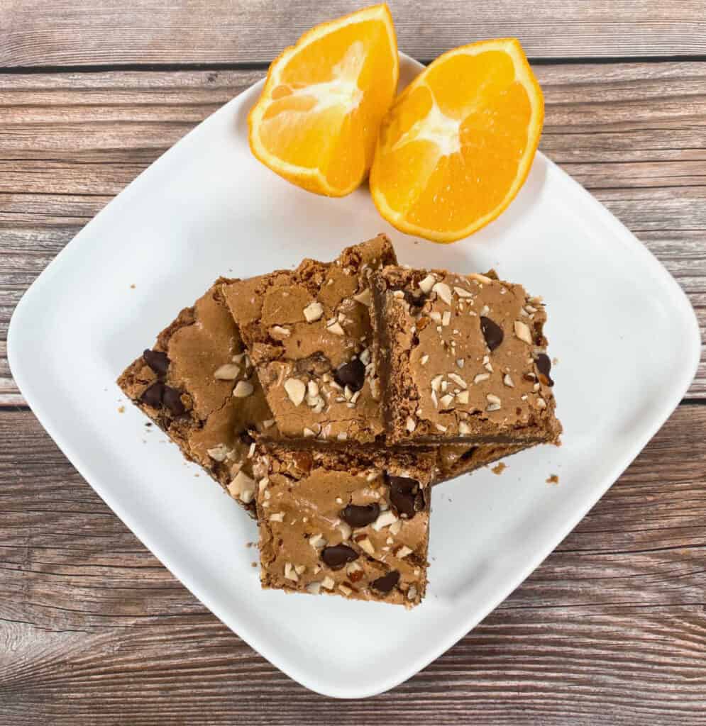 stacked almond orange brownies on a white plate with orange segments in the background 