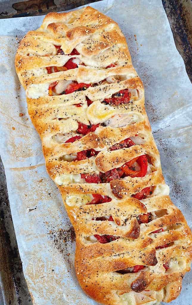 braided pizza dough filled with deli turkey, provolone cheese and roasted red peppers and topped with everything bagel seasoning sits on a parchment paper lined baking sheet. 