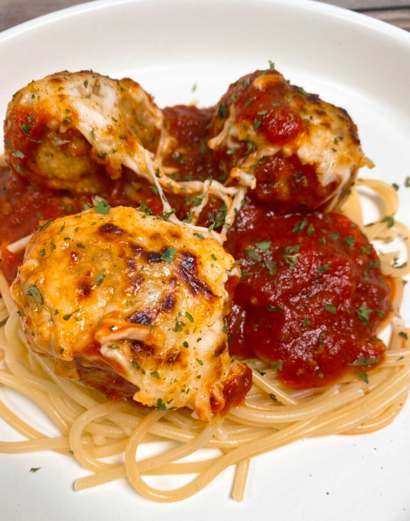 Browned cheese topped meatballs sit on a bed of pasta. 