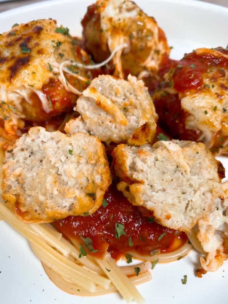 Close up image of halved meatballs, topped with cheese and sauce over pasta.