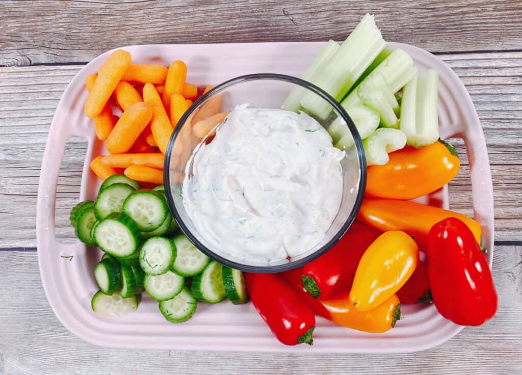 bowl of lighter veggie dip sits surrounded by carrots, celery, cucumbers and bell peppers