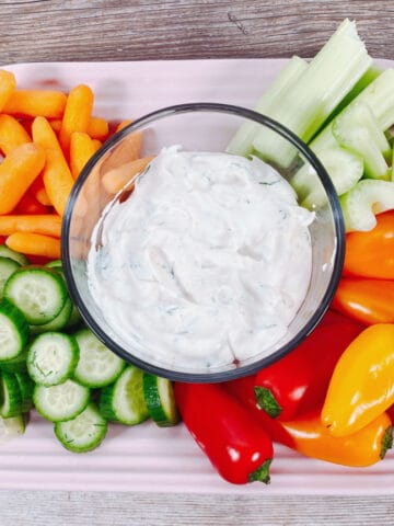 bowl of lighter veggie dip sits surrounded by carrots, celery, cucumbers and bell peppers