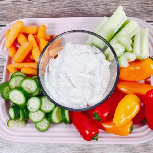 bowl of lighter veggie dip sits surrounded by carrots, celery, cucumbers and bell peppers