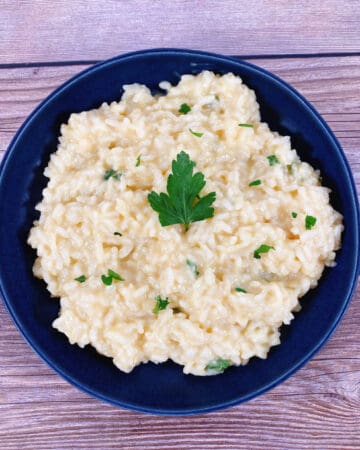 creamy parmesan risotto sprinkled with fresh parsley sits in a navy blue bowl on a wooden background